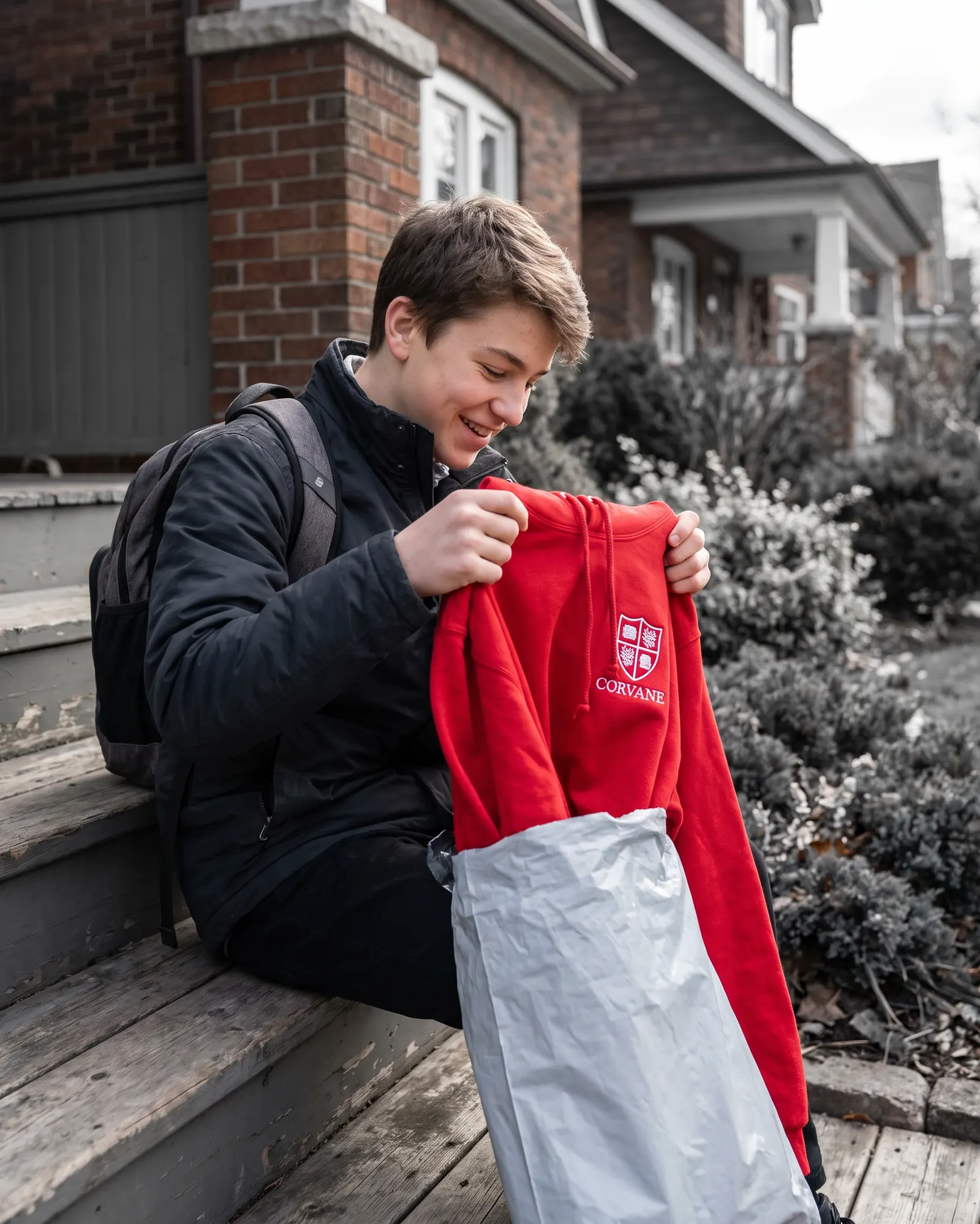 A young athlete pulling a red team hoodie out of a mailer at home.